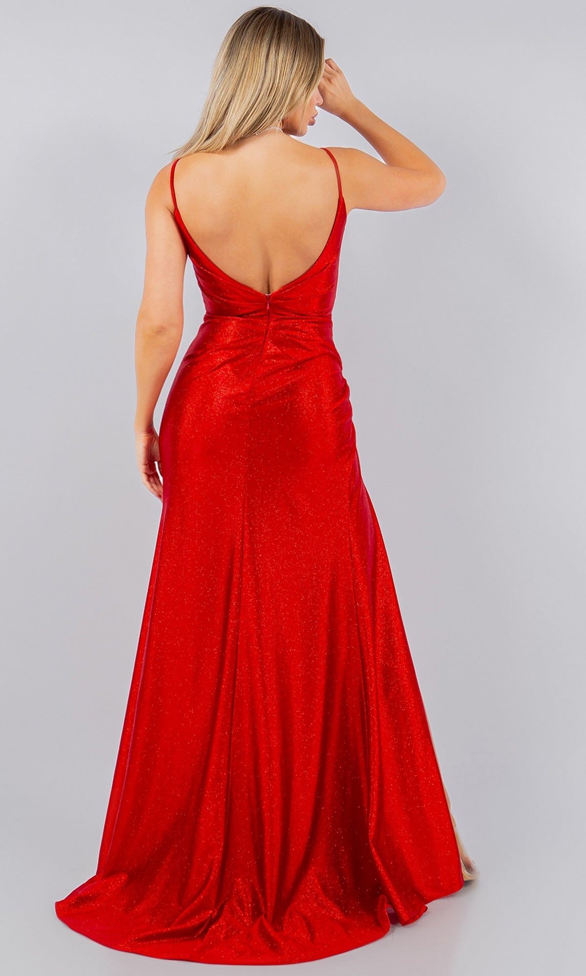 A woman stands with her back to the camera, wearing the Cinderella Couture 8117J—a floor-length, sleeveless metallic long prom dress with a deep V-back—set against a plain background.